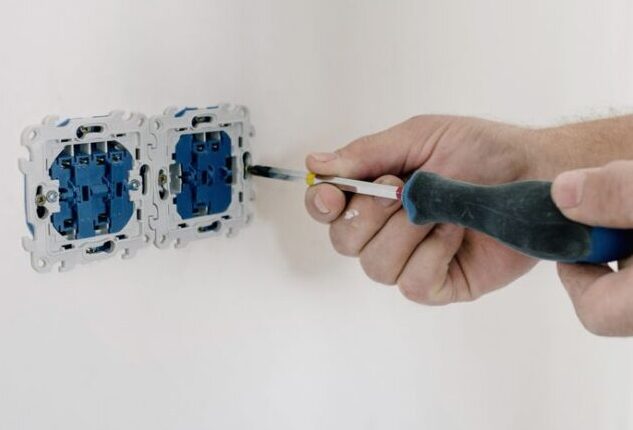 Crop faceless man using screwdriver for installation switches in apartment with light wall in daytime